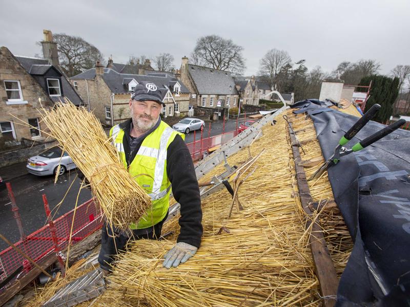 The final sheaf of wheat added to the roof of Burns Cottage in Alloway